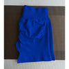 Shorts de yoga sans couture taille haute bleu royal posés à plat sur une surface marron texturée.