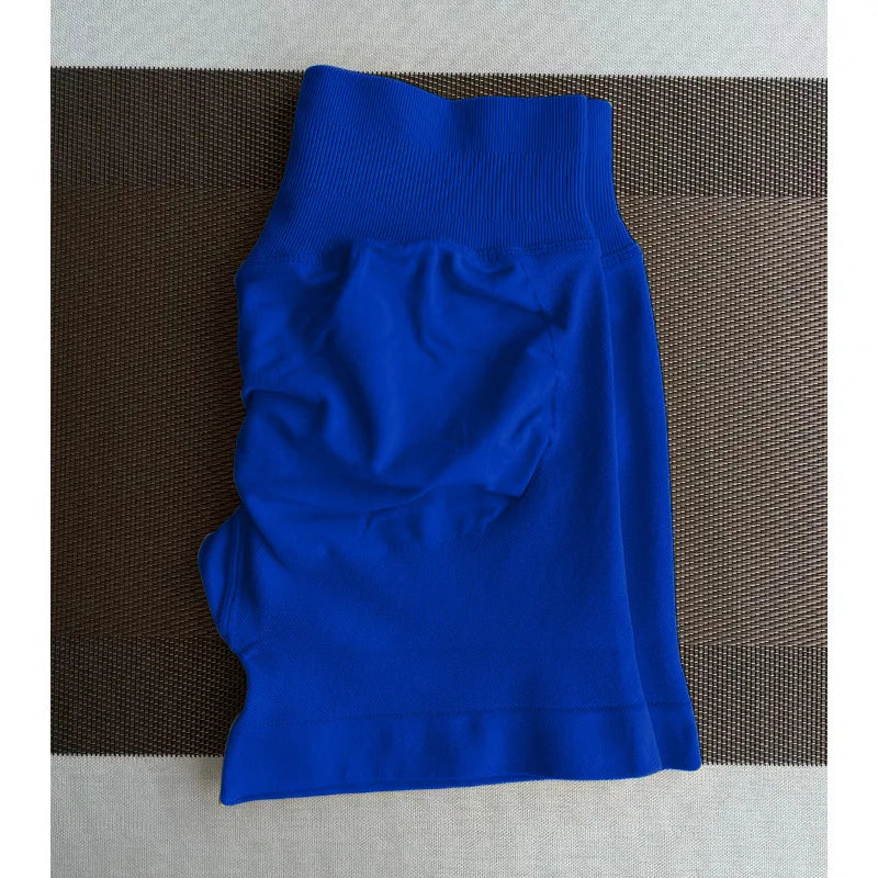 Shorts de yoga sans couture taille haute bleu royal posés à plat sur une surface marron texturée.