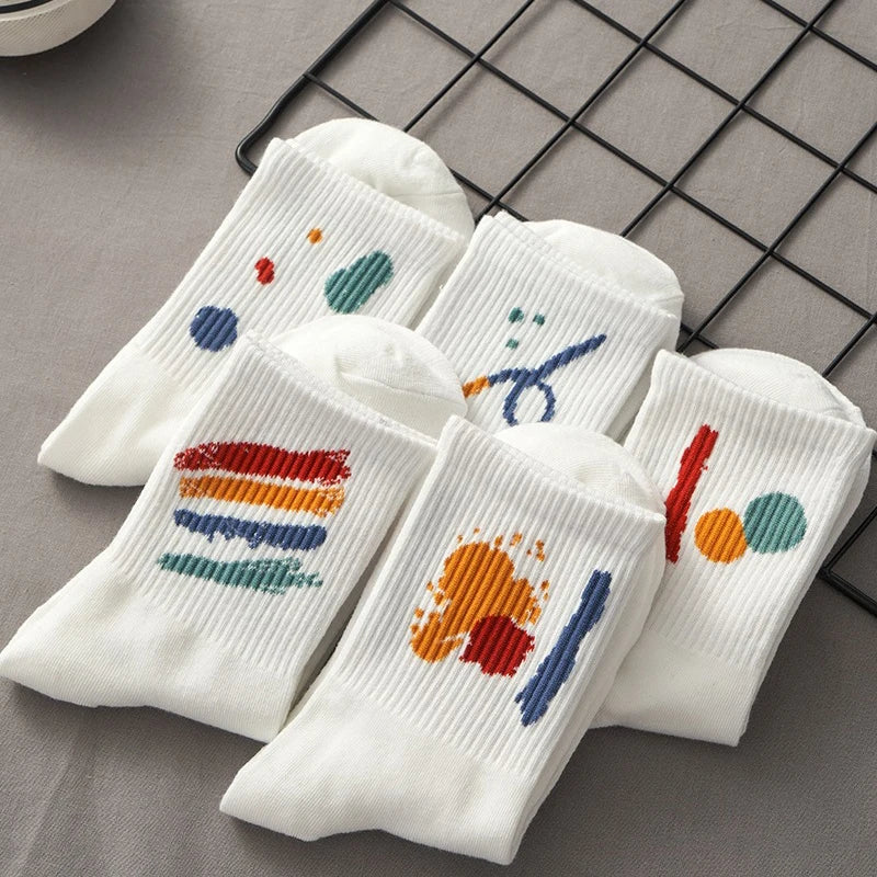 A stack of five white breathable cotton socks with colorful abstract patterns laid on a black wire grid.