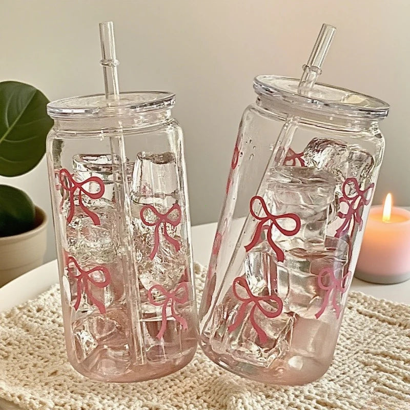 A clear tumbler filled with pink liquid and ice cubes, featuring a decorative pink bow design.