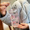 A hand holds a clear pink bow tumbler water bottle with a straw against a light gray quilted jacket.