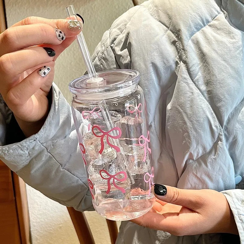 A hand holds a clear pink bow tumbler water bottle with a straw against a light gray quilted jacket.