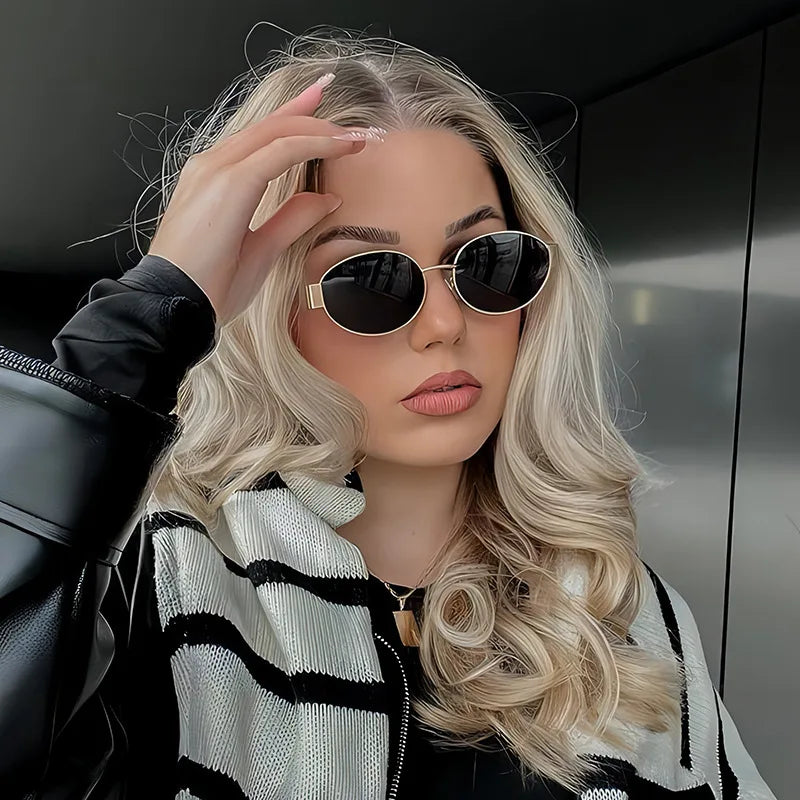 A woman with long blonde hair wearing classic oval metal sunglasses and a black and white striped jacket.