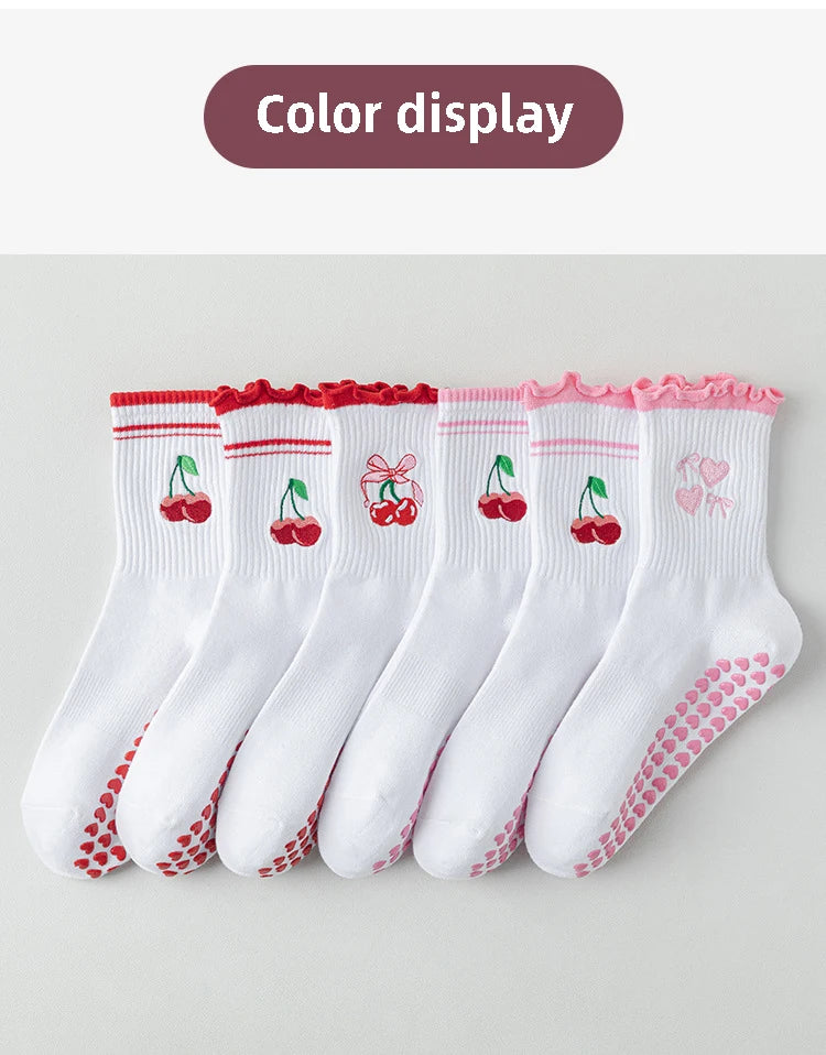 Une rangée de chaussettes de yoga blanches avec broderies rouges et roses et antidérapantes, présentées sur un fond clair.
