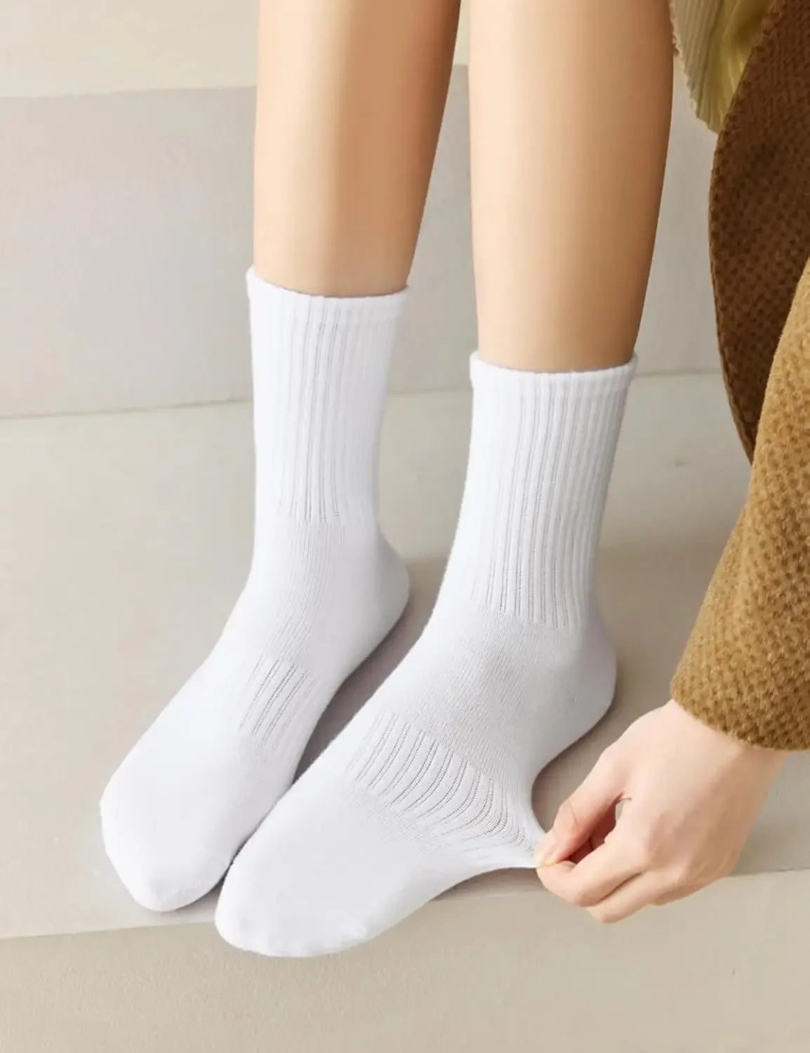 Une paire de chaussettes en coton côtelé blanc tenue par une main contre une surface claire.