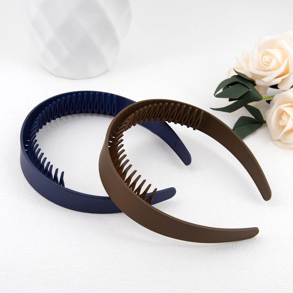 Eine braune Plastik-Haarbandseite neben einer blauen auf einer weißen Oberfläche mit einer hellrosa Rose.