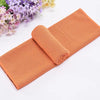 Serviette de refroidissement orange circulaire roulée à côté de fleurs violettes sur fond blanc.
