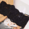 Primer plano de una prenda de encaje negro drapeada sobre una canasta tejida, con las manos de una persona visibles.