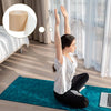 A woman performs a stretch exercise using a foam elastic skin bandage on a teal yoga mat.