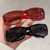 A pair of red and black Y2K cat eye rhinestone sunglasses being held in a hand.