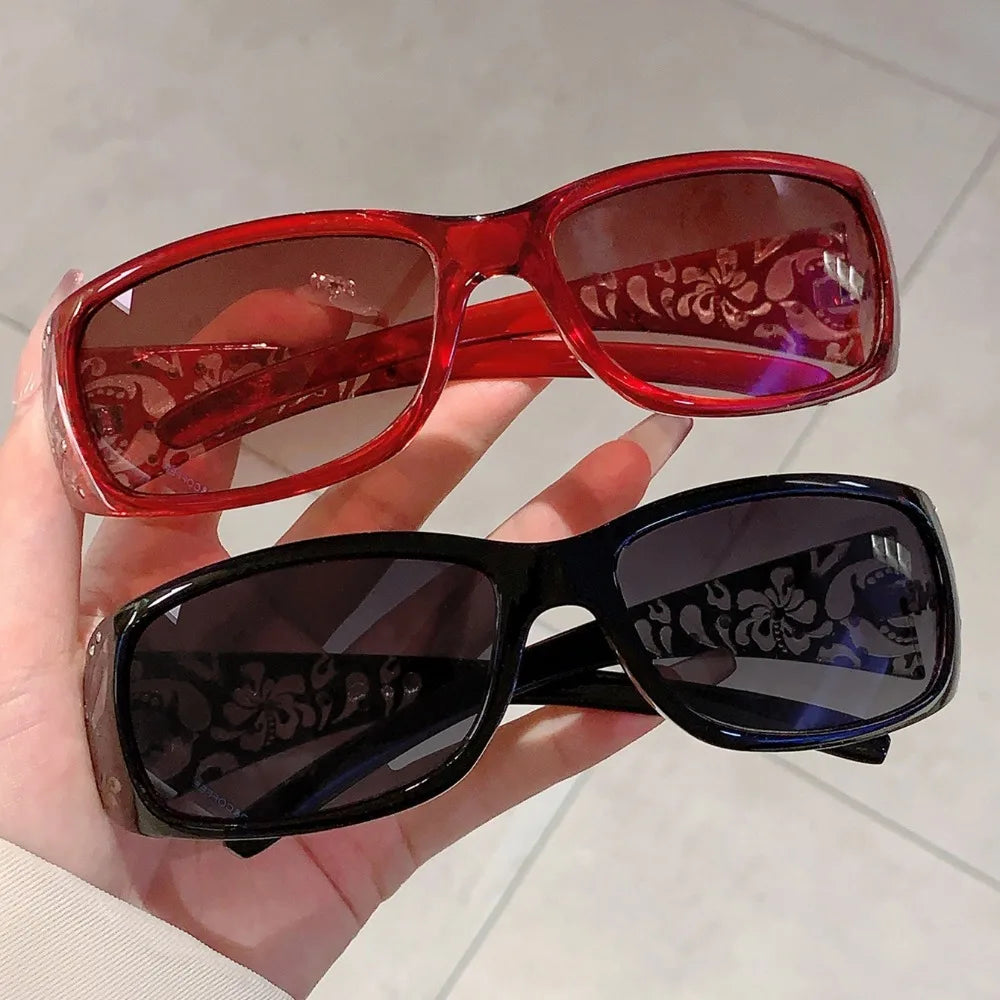 A pair of red and black Y2K cat eye rhinestone sunglasses being held in a hand.