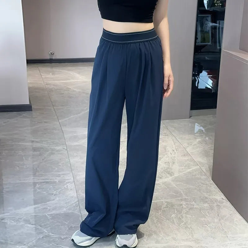 A woman wearing dark blue loose sports yoga pants and a black top standing indoors.