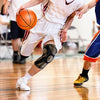 A person wearing a black knee brace is playing basketball on a wooden court.