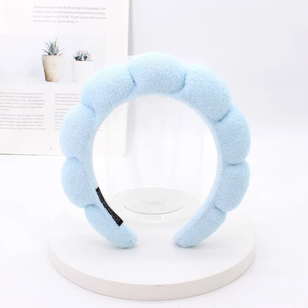 Light blue sponge terry cloth headband for hair styling displayed on a white circular stand.