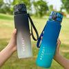 A hand holds a gradient blue sports water bottle with a black cap outdoors.
