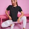 A woman wearing a black breathable summer yoga and fitness t-shirt and white pants sitting on a pink bench.