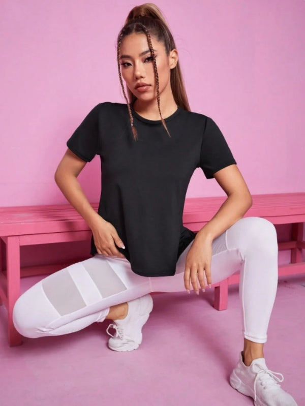 Una mujer vistiendo una camiseta deportiva de yoga y fitness negra transpirable y pantalones blancos, sentada en un banco ros