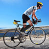 A man rides a bicycle outdoors wearing black compression socks and a yellow helmet.