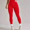 Eine Frau trägt rote, hochtaillierte, nahtlose Yoga-Leggings und ein weißes Oberteil, steht drinnen.