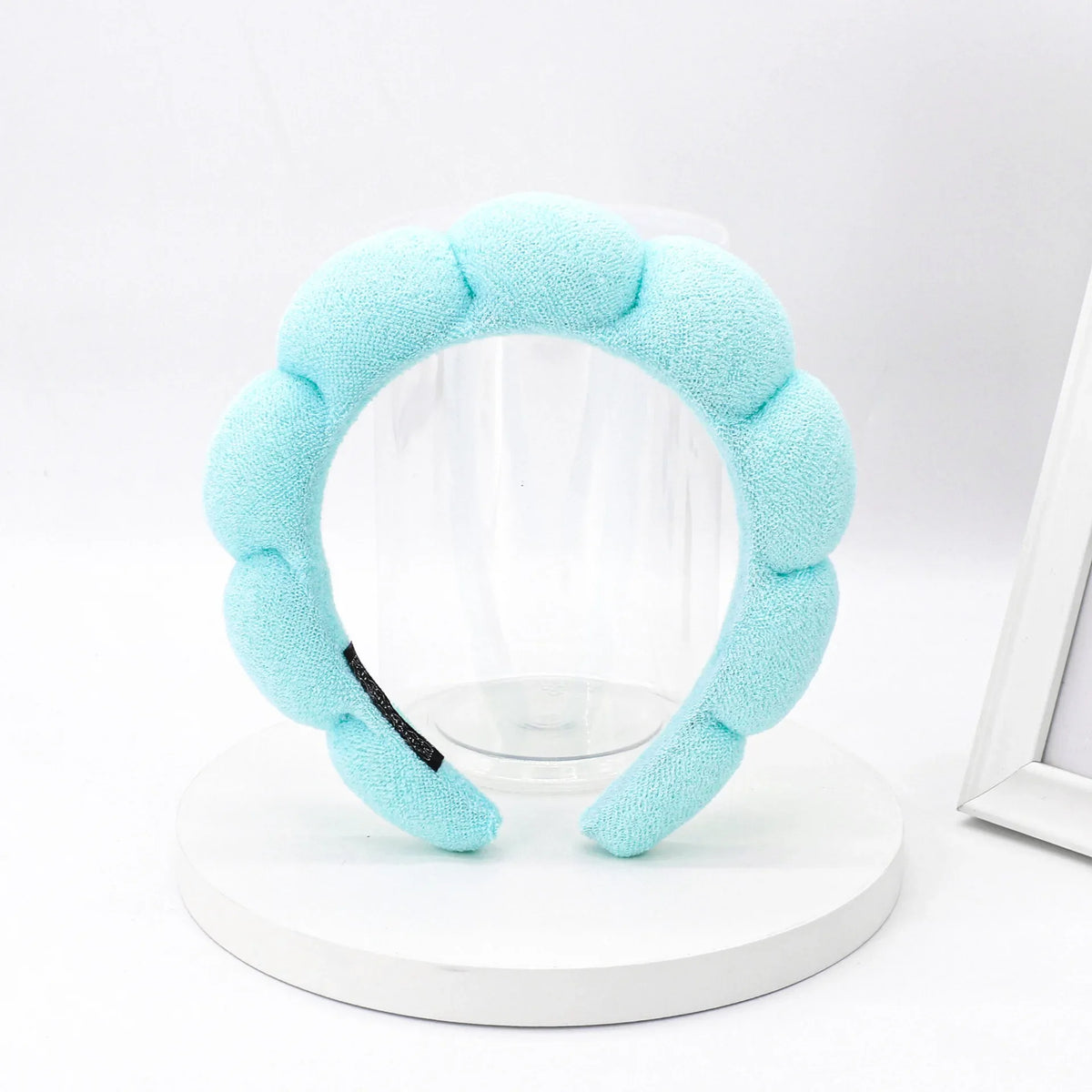 Light blue sponge terry cloth headband for hair styling displayed on a white stand.