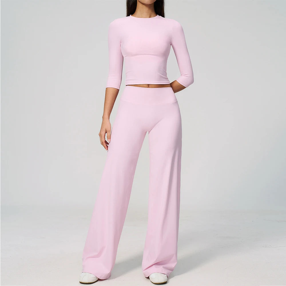 A woman wearing a light pink long-sleeved top and matching high-waisted leggings set for yoga or fitness.