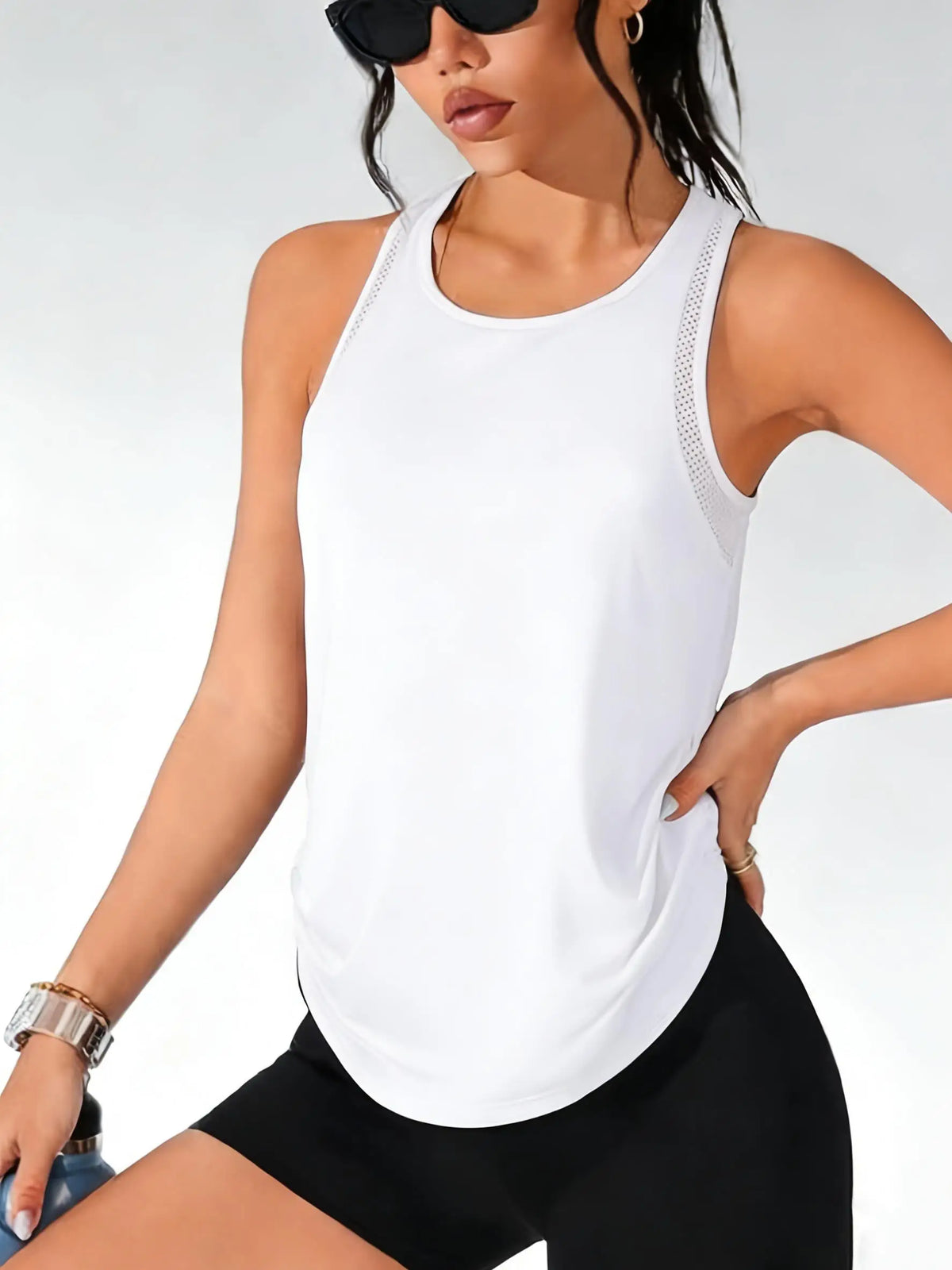 A woman wearing a white breathable sport tank top and black athletic bottoms.