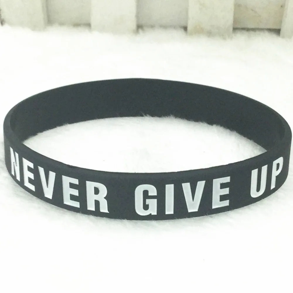Bracelet silicone noir avec l'inscription NEVER GIVE UP, posé sur une surface blanche.