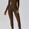 Model in a dark brown, long-sleeved, high-neck yoga jumpsuit and white sneakers.