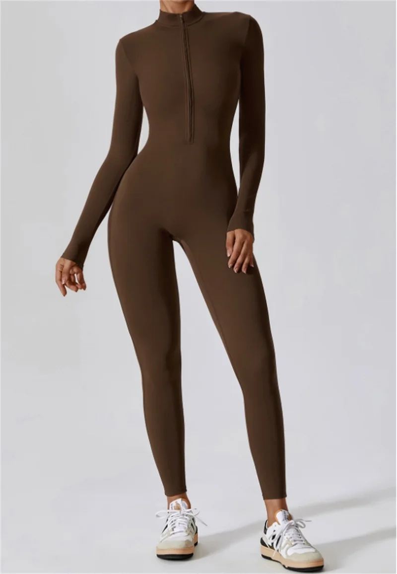 Model in a dark brown, long-sleeved, high-neck yoga jumpsuit and white sneakers.