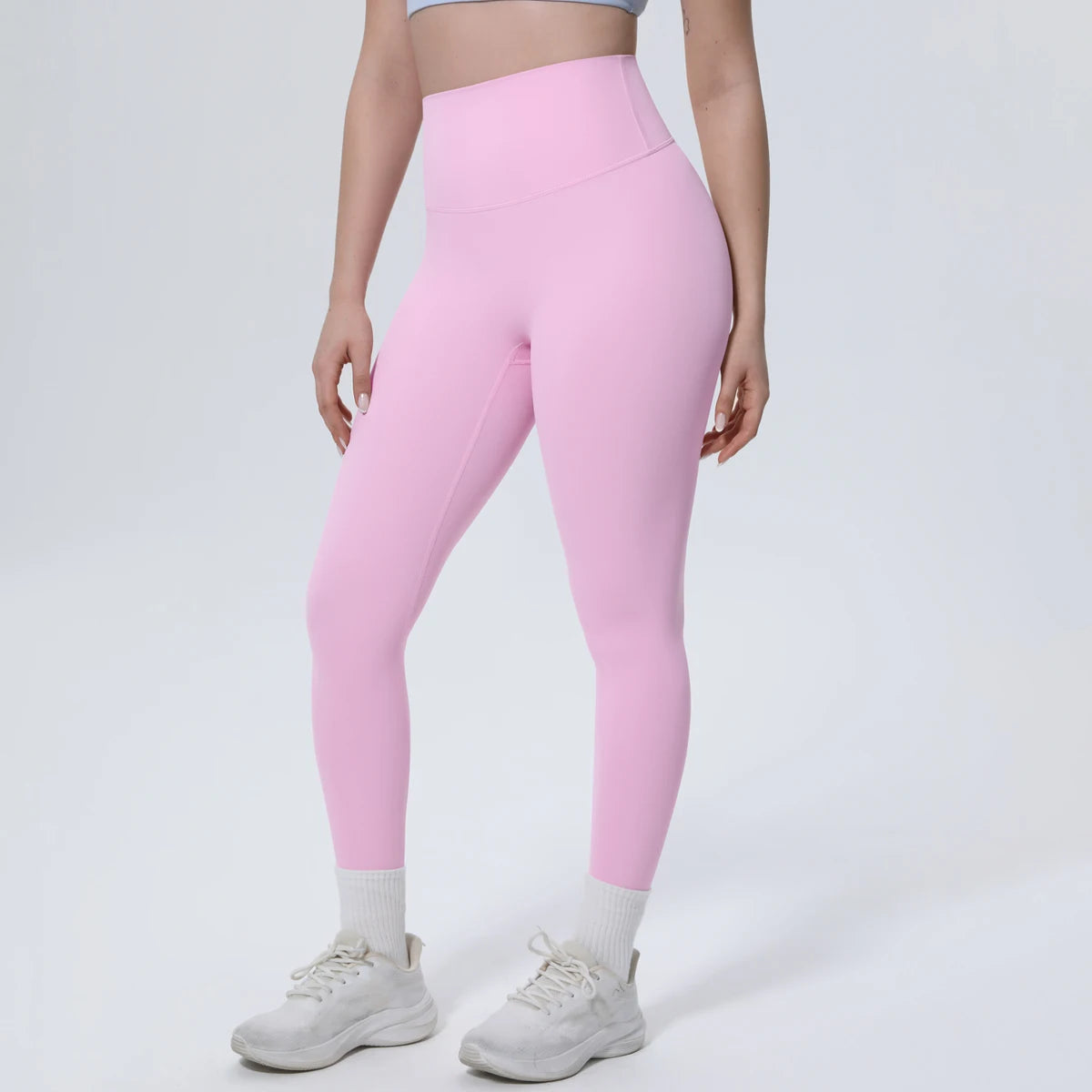 A model wears pink high-waisted yoga leggings and white sneakers.