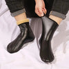 A pair of black leather boots with tan sherpa lining are shown being worn on a person's foot.