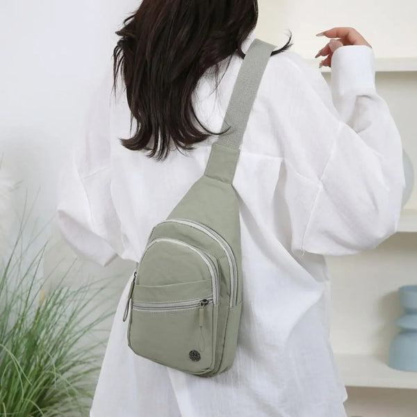 A light green durable crossbody messenger bag worn by a person in a white shirt.