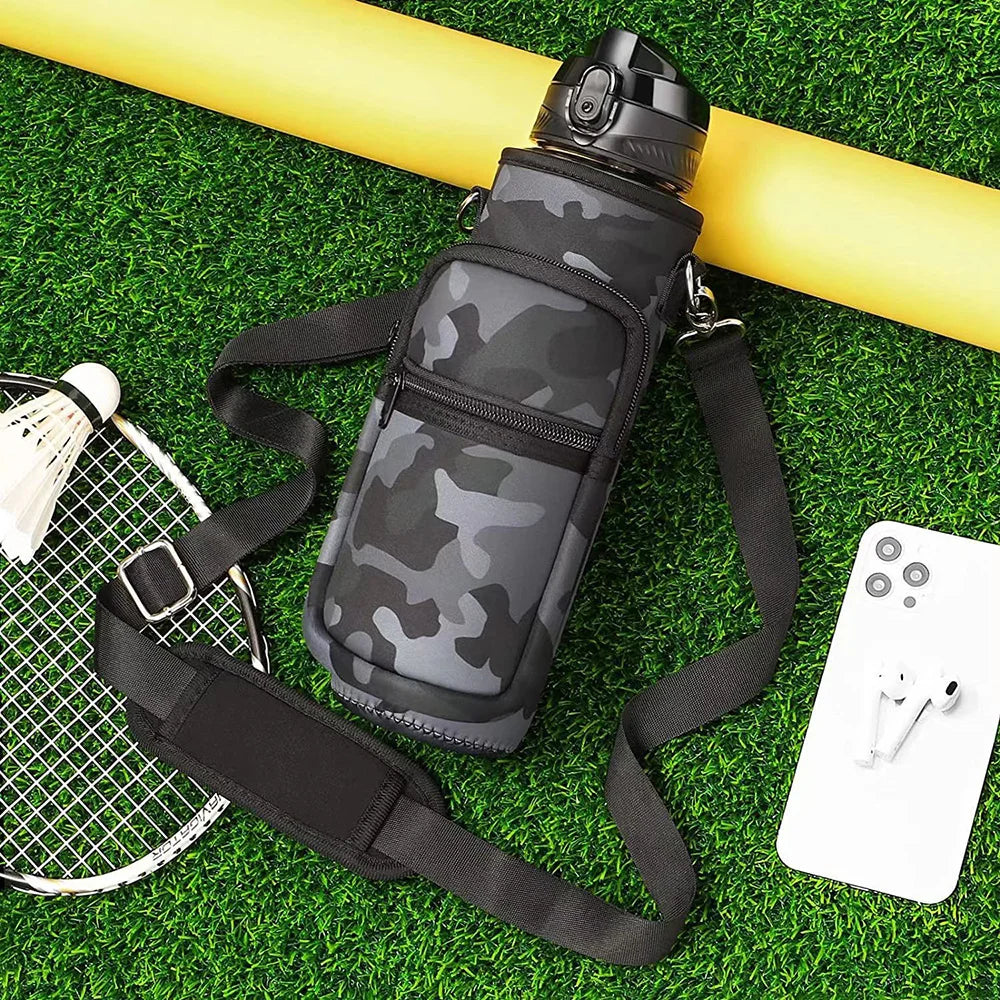 Botella térmica camuflada con funda y correa sobre césped verde junto a una raqueta de tenis.