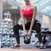 Eine Frau in einem pinken Sporttop und schwarzen Leggings führt eine Kniebeuge mit doppelten Schaumstoffknieschützern aus.