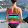Back view of a woman wearing a color-block zigzag three-piece swimsuit set with pink, black, and neon accents by the sea.