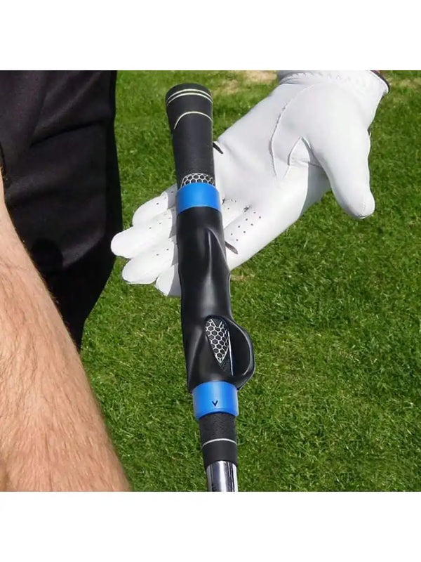 A close-up of a black golf club grip trainer with blue accents being held by a gloved hand on a green grass surface.