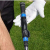 A close-up of a black golf club grip trainer with blue accents being held by a gloved hand on a green grass surface.
