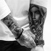 A black and white photo showing a person's arm with a detailed tattoo of a woman's face and a black wristband.