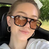 Una mujer con gafas de sol cuadradas y ligeras, tintadas en marrón, sentada en un coche.