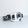 A pair of white and black sport-grade skiing goggles with a clear lens resting on a gray surface.