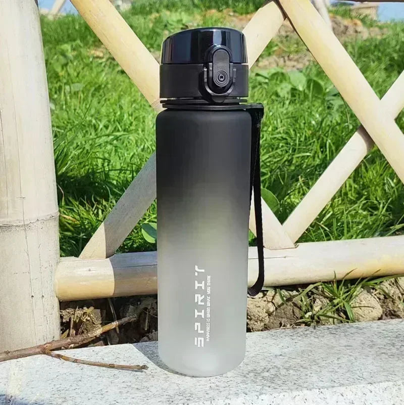 A clear sports water bottle with a black cap standing on a stone surface outdoors.