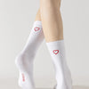 A person is wearing white crew socks with red heart designs on their legs.
