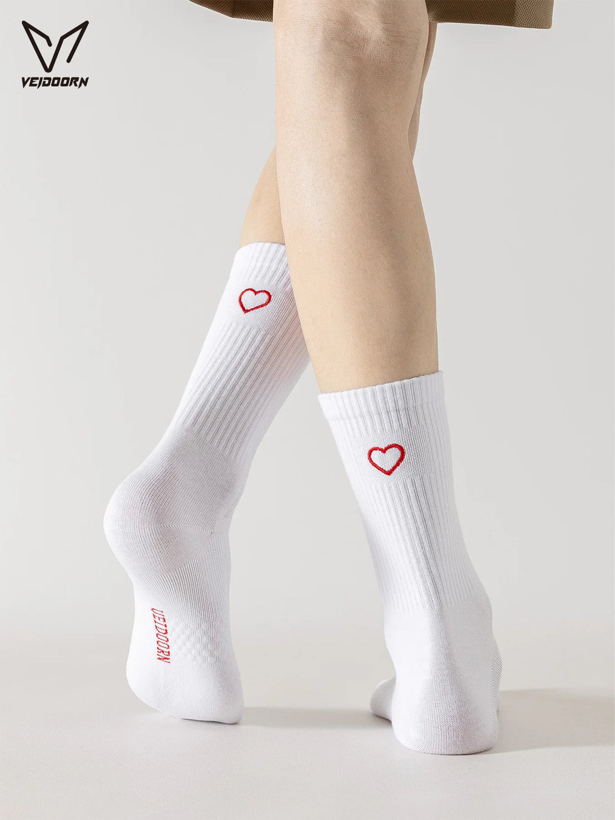A person is wearing white crew socks with red heart designs on their legs.