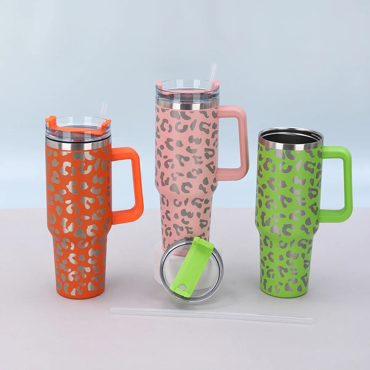 Trois tasses en acier inoxydable isothermes orange, rose et vert lime avec motifs léopard.