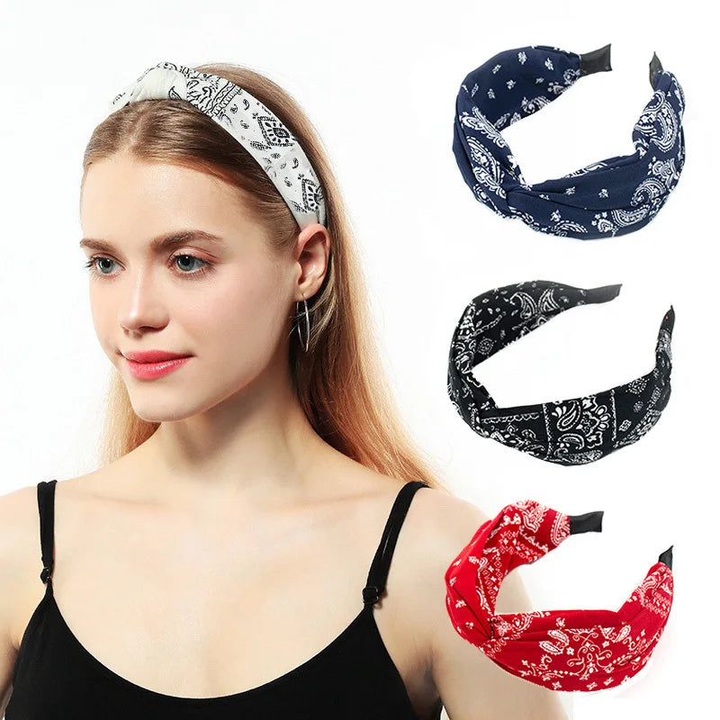 Una mujer modela varios accesorios para el cabello de tela, incluyendo una diadema estampada, una bandana oscura y una bufand