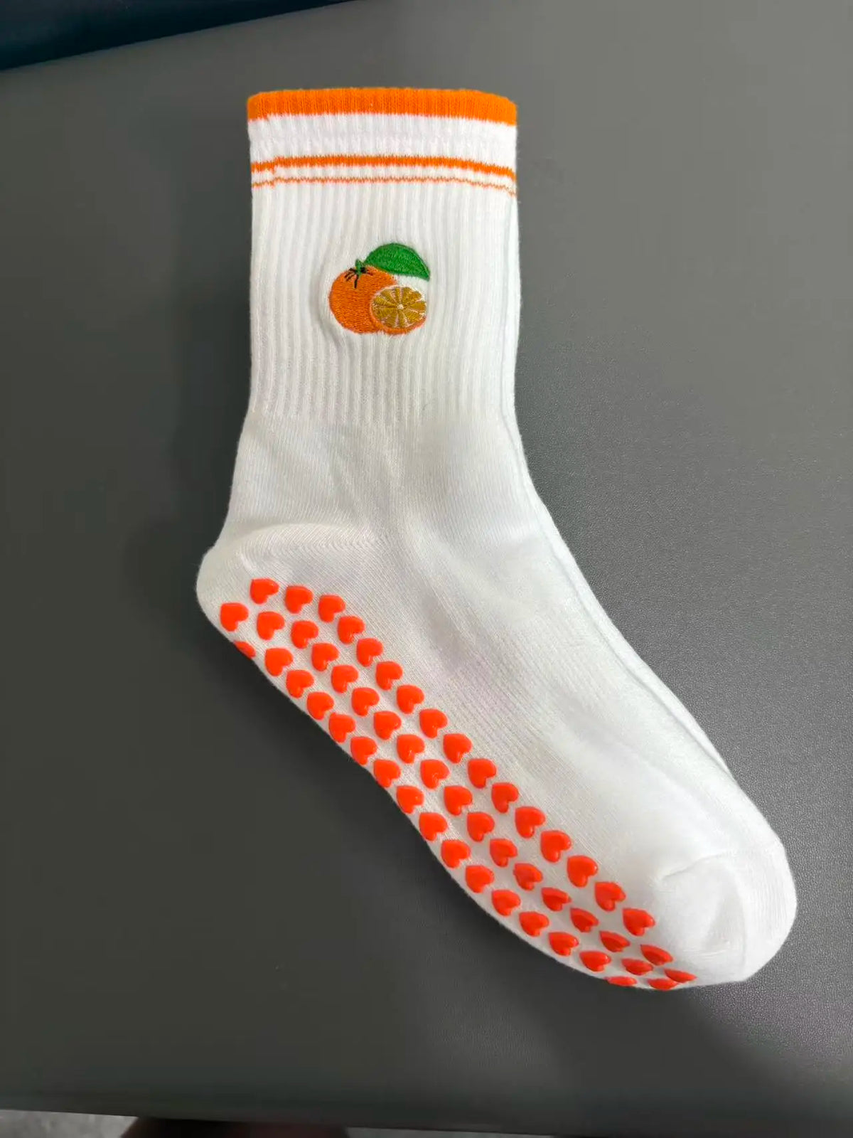 Weiße Strick-Yoga-Socken mit orangen Streifen und einem kleinen orangen Zitrusfrucht-Design an der Zehenpartie.