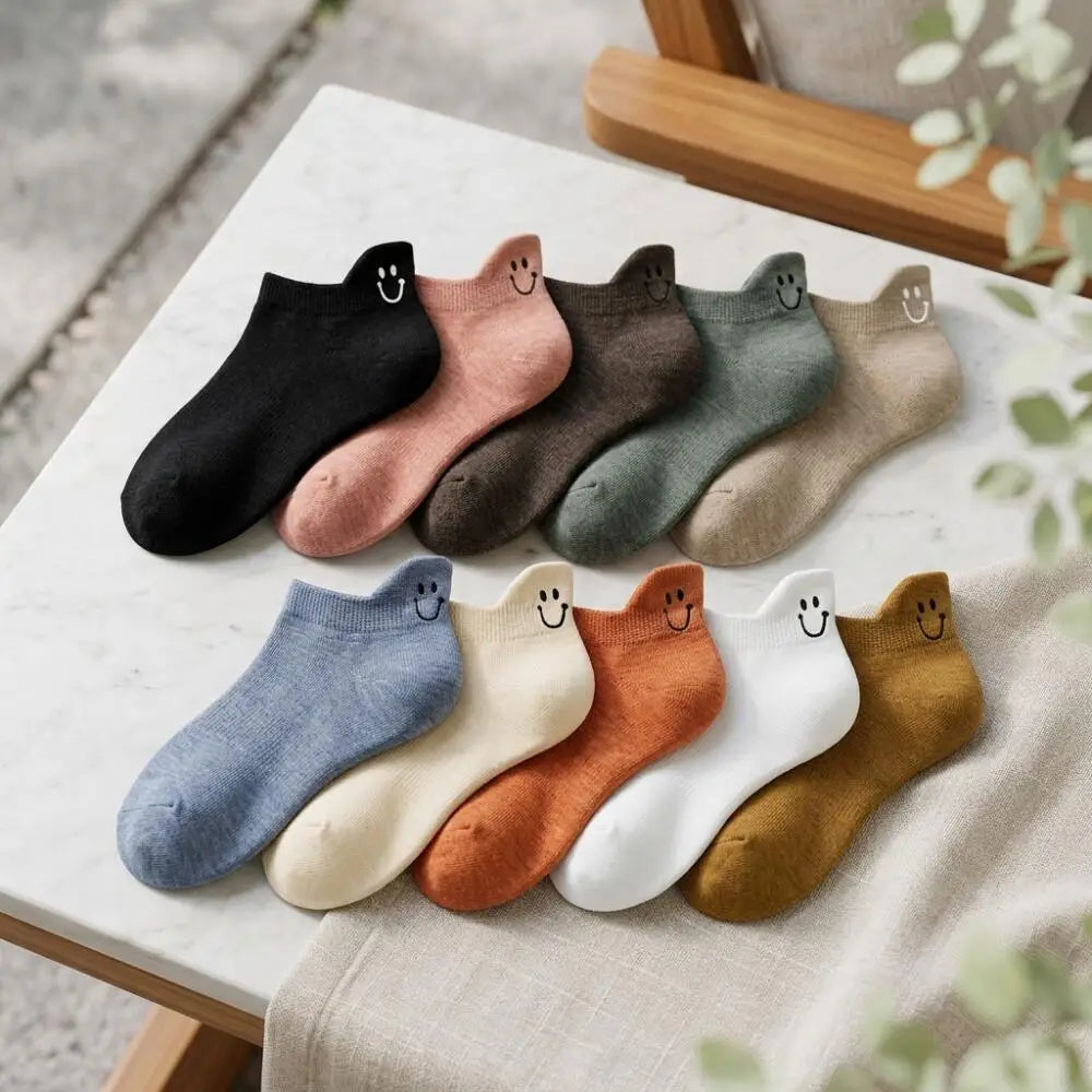 An assortment of eight low-cut ankle socks with smiling embroidery displayed on a white marble surface.