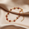 Gold charm bracelet featuring round evil eye beads with red and white designs on a soft beige fabric.