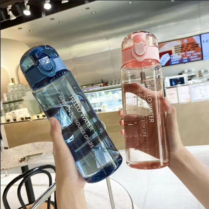 A hand holds a clear blue sports water bottle filled with water in a bright indoor setting.