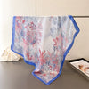 A light blue and pink floral silk scarf draped on a gray surface.